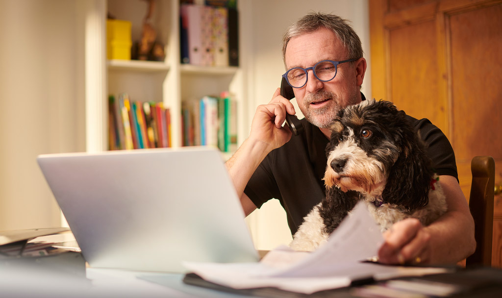 smiling man holding phone with laptop open and dog on lap